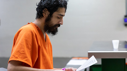 A person with an orange jail jumper, holding and reading from a piece of paper