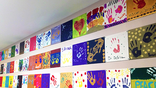 Angled interior shot of a wall filled with children's colorful finger-paint pictures on construction paper