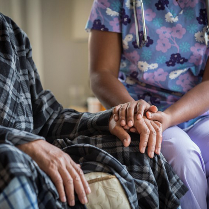 A photo depicting a staff member at a care facility gently grasping the hand of an elderly man as if to comfort him