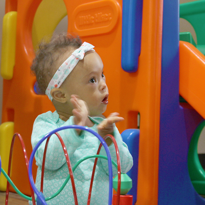 An infant girl in a play room clapping her hands.