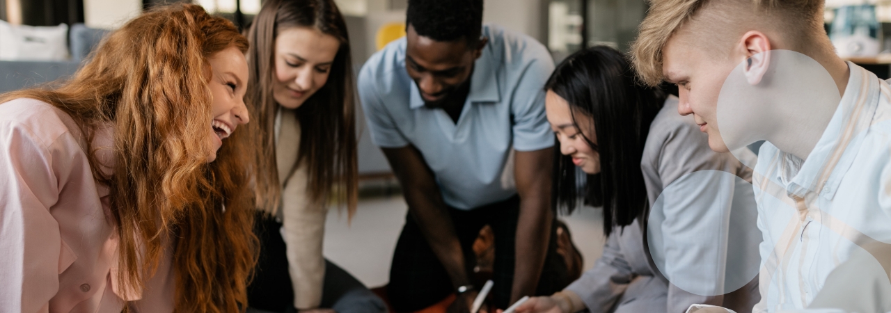 Diverse group of young co-workers engaged and working, leaning in a semi-circle around a table