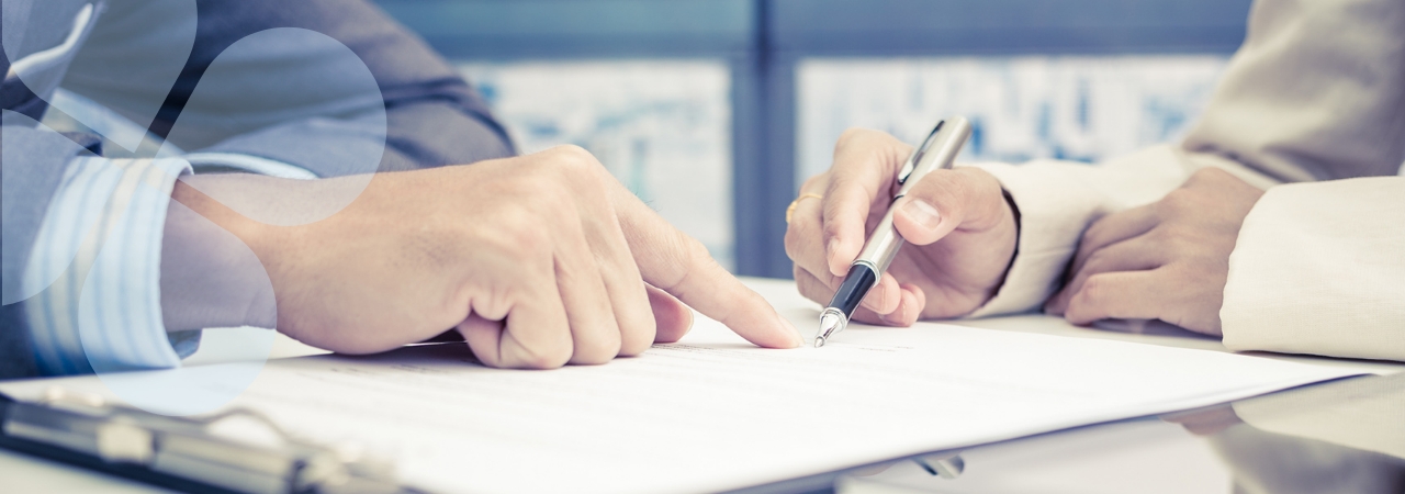 Closeup of one business person guiding another through signing contract forms