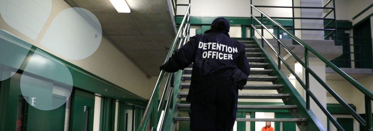 Detention Center guard ascending stairs with inmate looking on in the distance