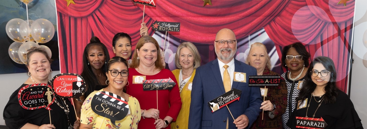 Harris Center staff in a decorated space, smiling for a group pic and holding career-realted signs