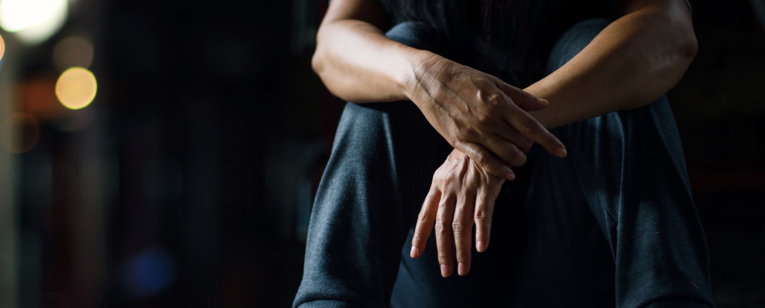 Close-up of a person sitting with hands clasped, conveying a sense of stress or contemplation in a dimly lit environment.
