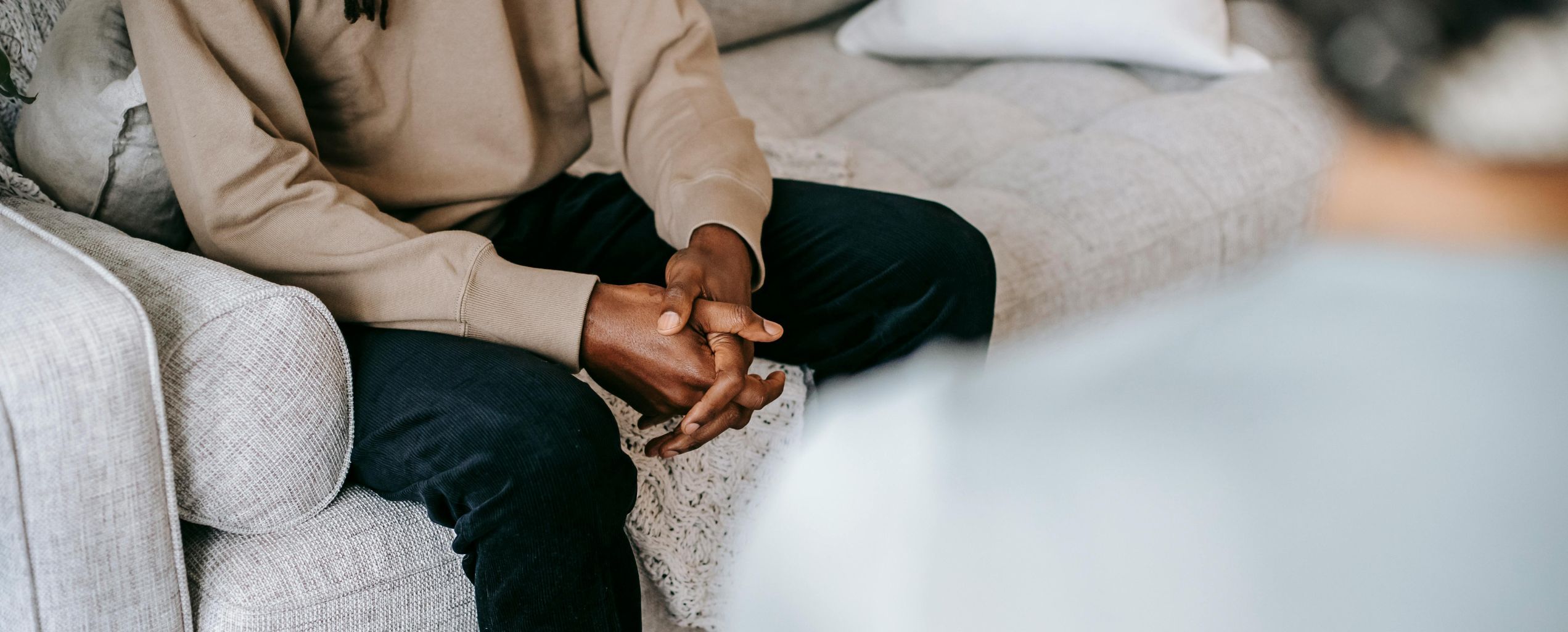 Person sitting on a couch with hands clasped together, suggesting a counseling or therapy session