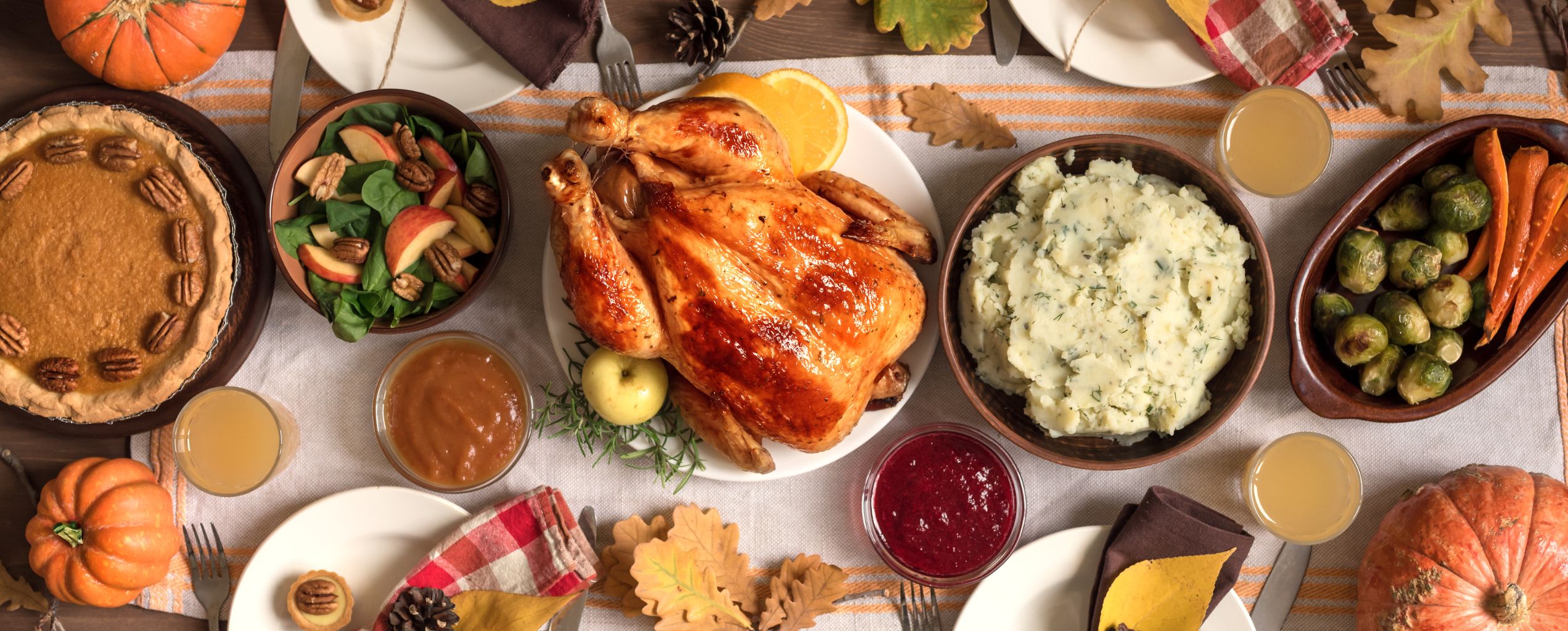 A festive Thanksgiving dinner table with a roasted turkey, mashed potatoes, roasted vegetables, salad, pumpkin pie, and seasonal decorations like pumpkins and autumn leaves.