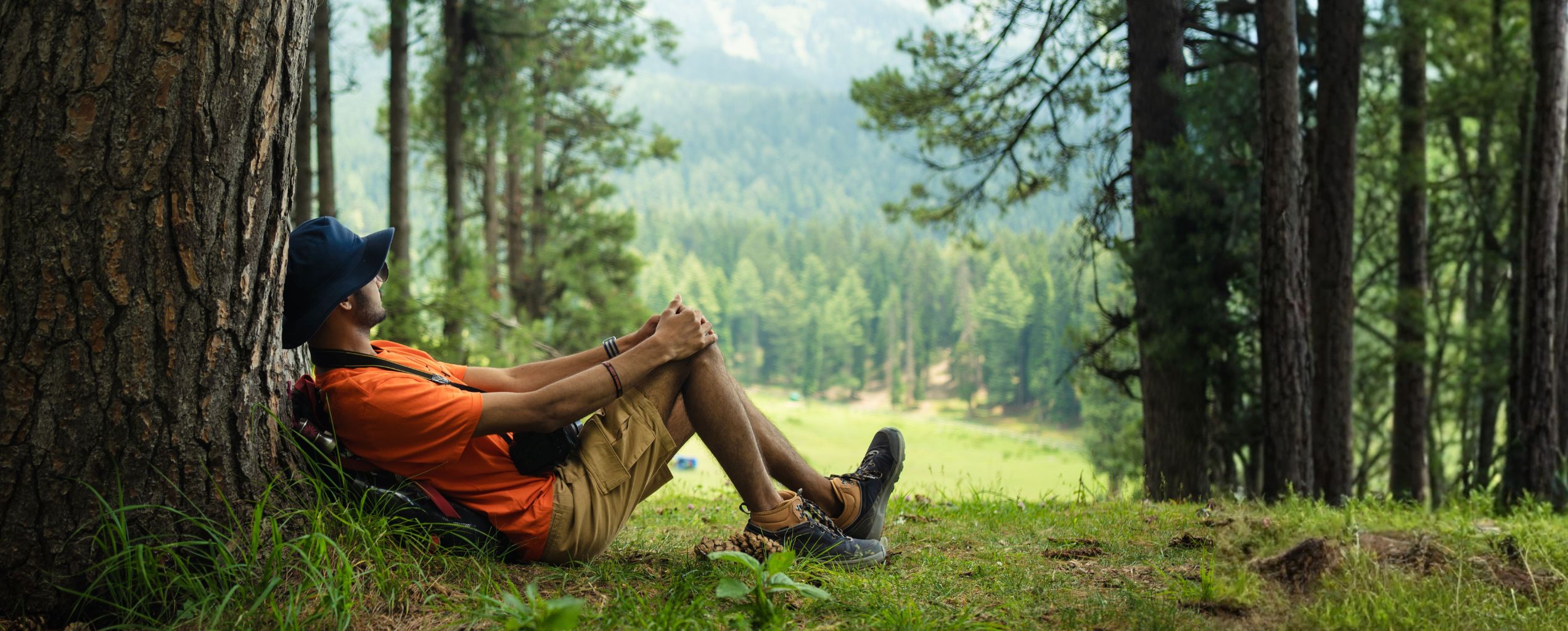 Hiker leaning against a tree in nature, relaxing.