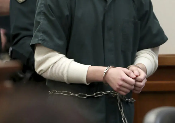 Close shot of convict's hands bound with cuffs and chain in a courtroom setting