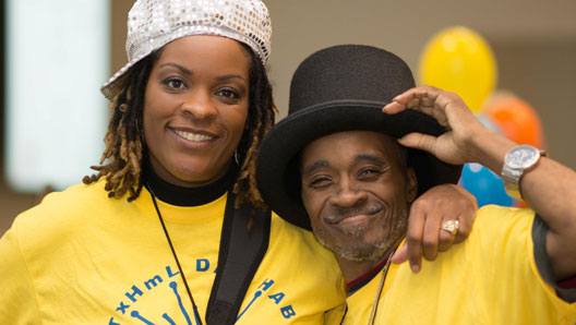 Harris Center Texas Home Living (TxHmL) staff member and client posing for a portrait, wearing hats with character and matching program shirts