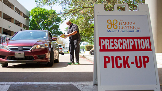 A Harris Center staff member assisting a client in their car, with a Prescription Pick-up sign in the foreground