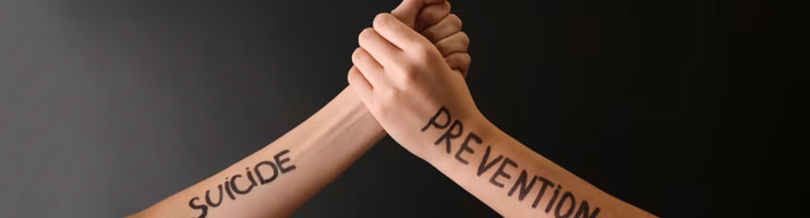 Two arms, one with the word "Suicide" and the other with the word "Prevention" written on them, with hands joined in a symbol of teamwork.