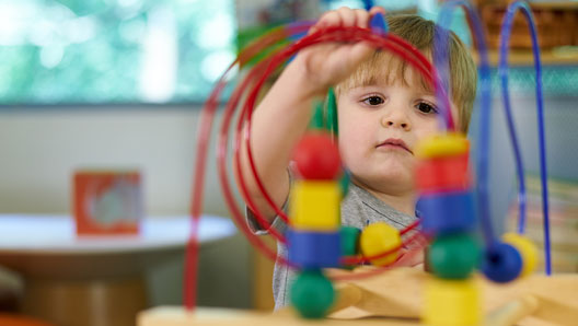 Young boy concentrating on a toy with wood blocks strung on looping metal rods