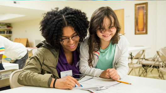 An adult and child, smiling and working on a project in a classroom setting