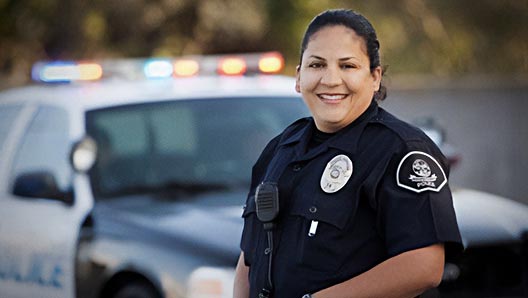 Portrait of smiling law officer standing in front of squad car with its lights on