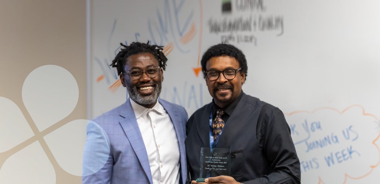 Two people standing in a classroom setting holding an award for outstanding achievement/service