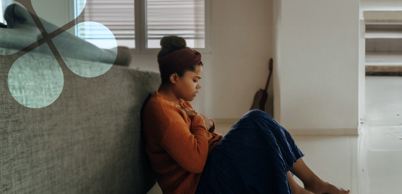 A teenager sits on the floor in a home setting, appearing distressed